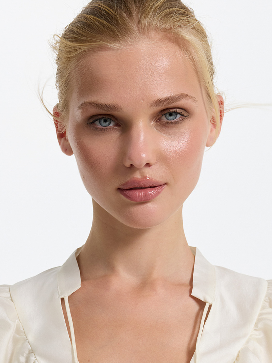 Before retouch — blonde model with blue eyes in white satin blouse, natural skin with slight imperfections