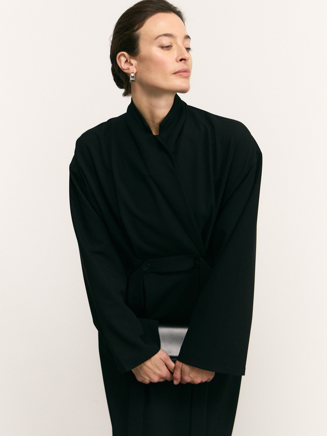Before retouch — model in black wrap blazer with silver-satin accent, cream background