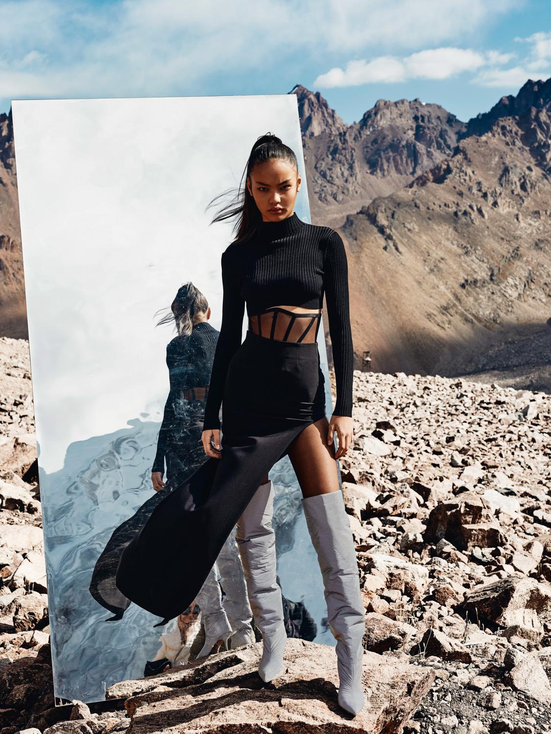 Before retouch — model in black ribbed crop set and white knee boots in rocky mountain landscape with mirror prop