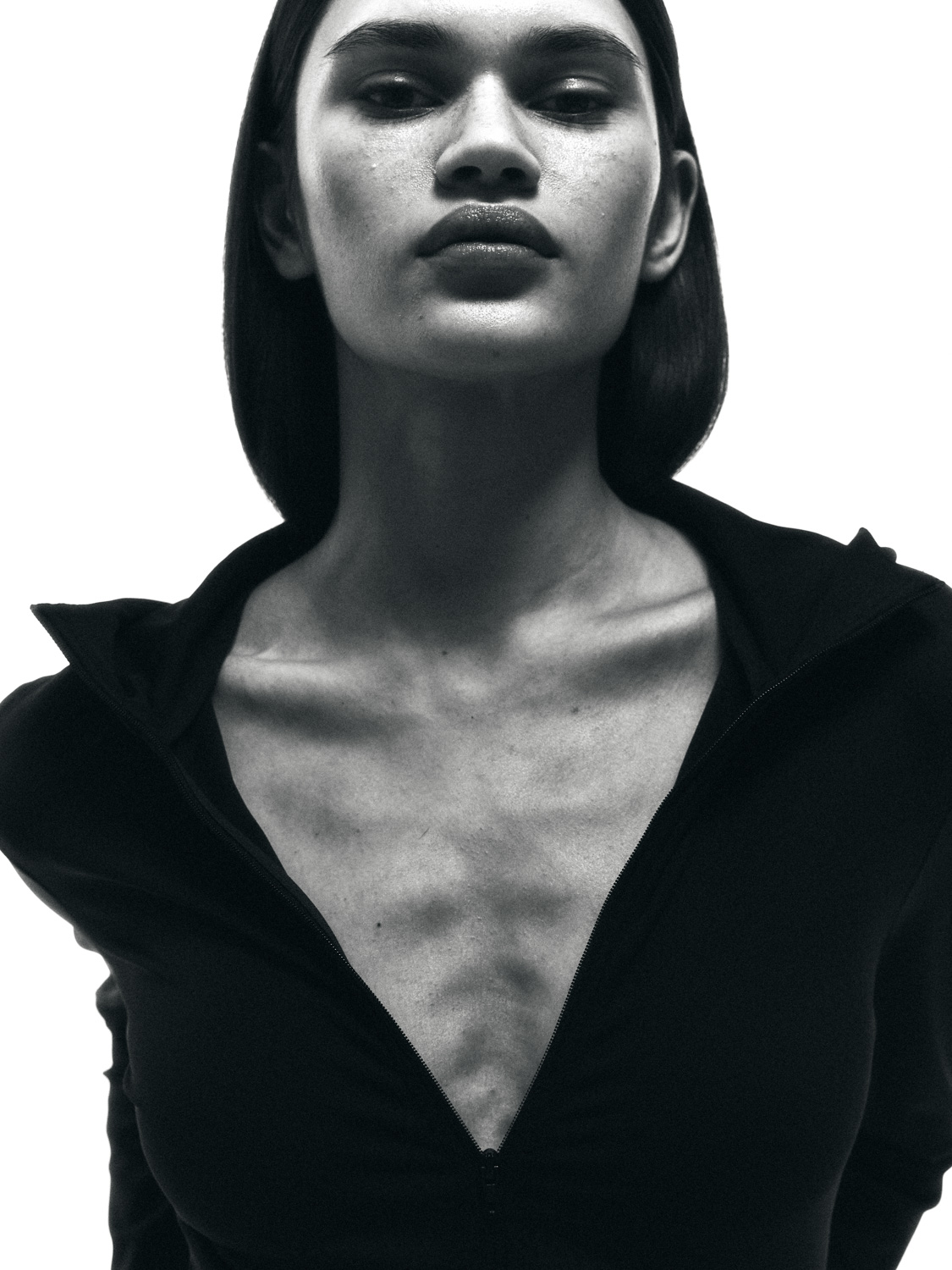 Before retouch — B&W close-up of model in black zip hoodie, visible skin texture and veins on chest and décolleté