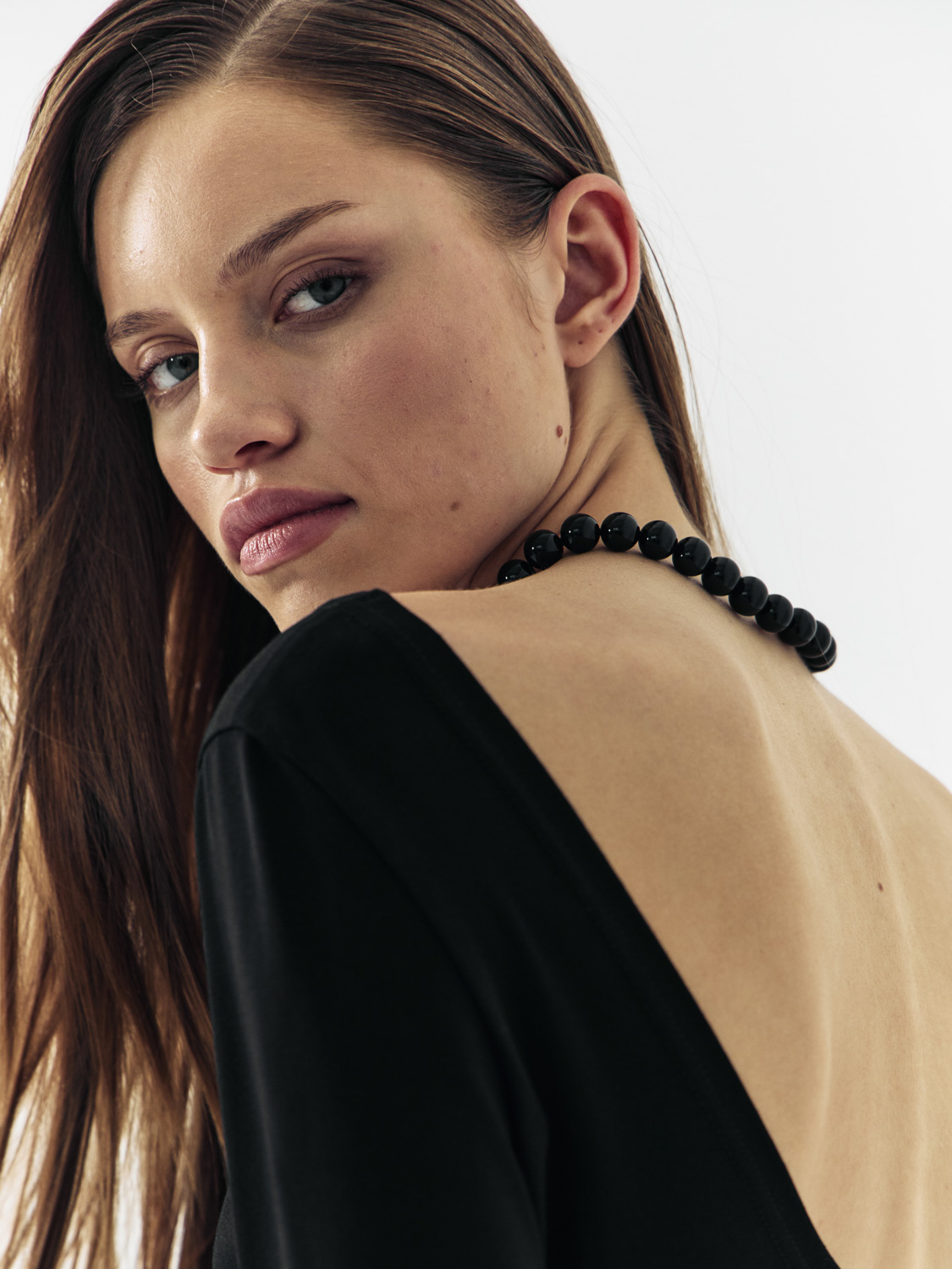 Before retouch — model with black bead necklace looking over shoulder, black and beige top, slight skin imperfections