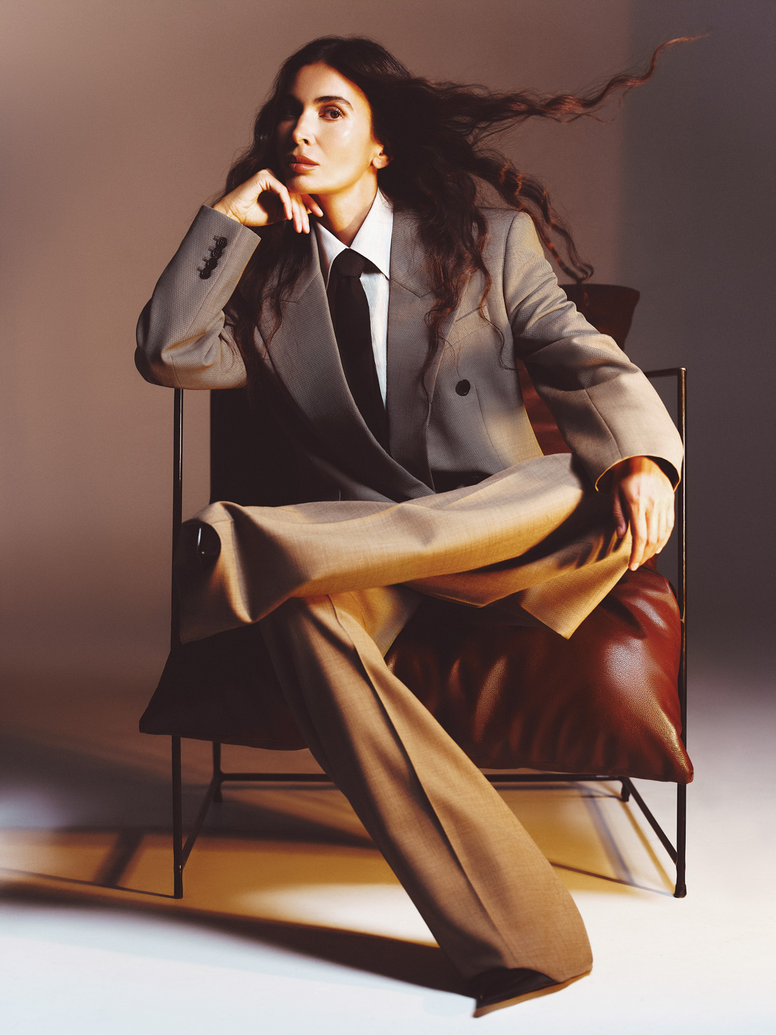for Moskvichka magazine — woman in black sleeveless dress seated, dark curly hair, warm amber studio