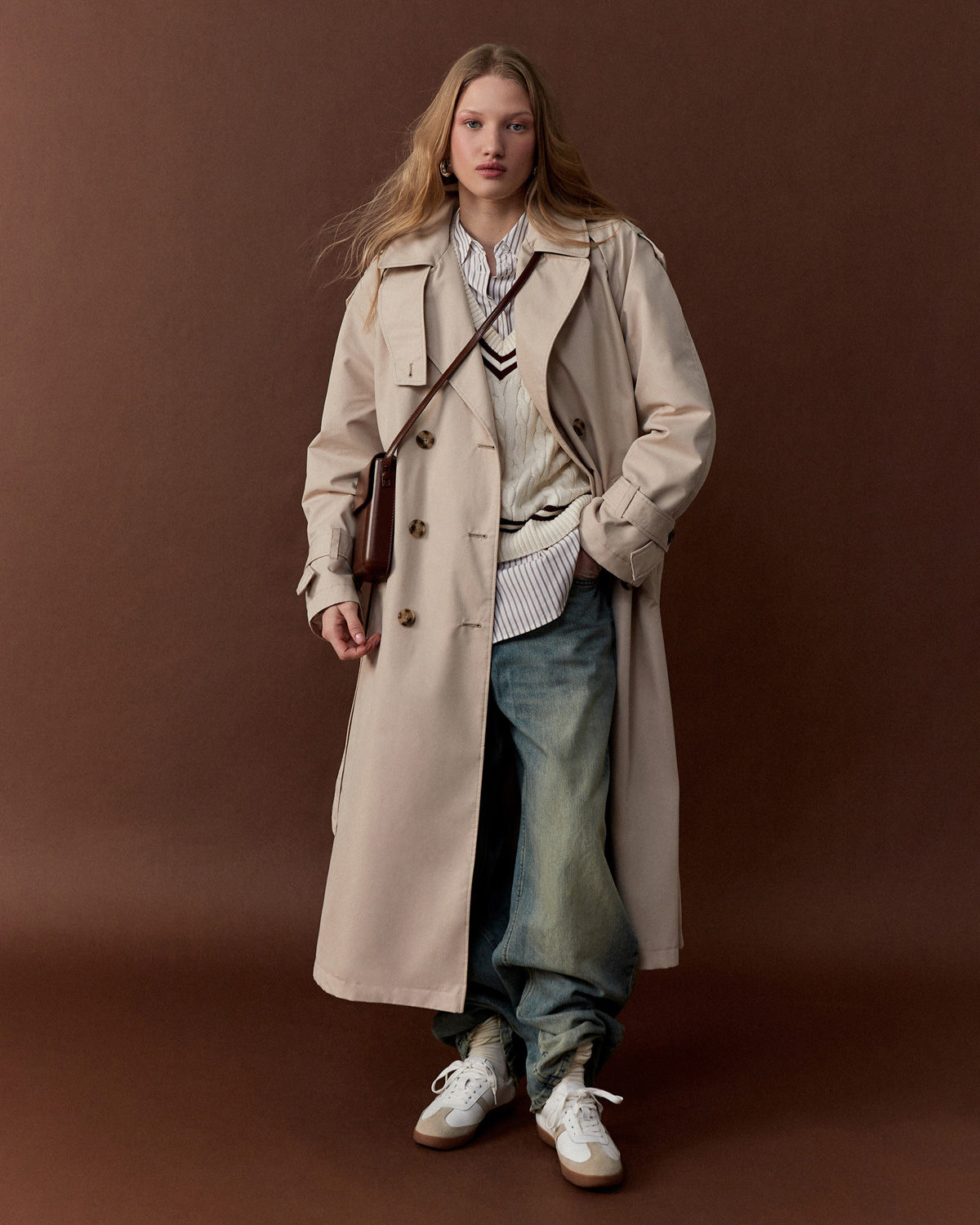 Onlyme — model in beige trench coat with jeans and white sneakers, brown background