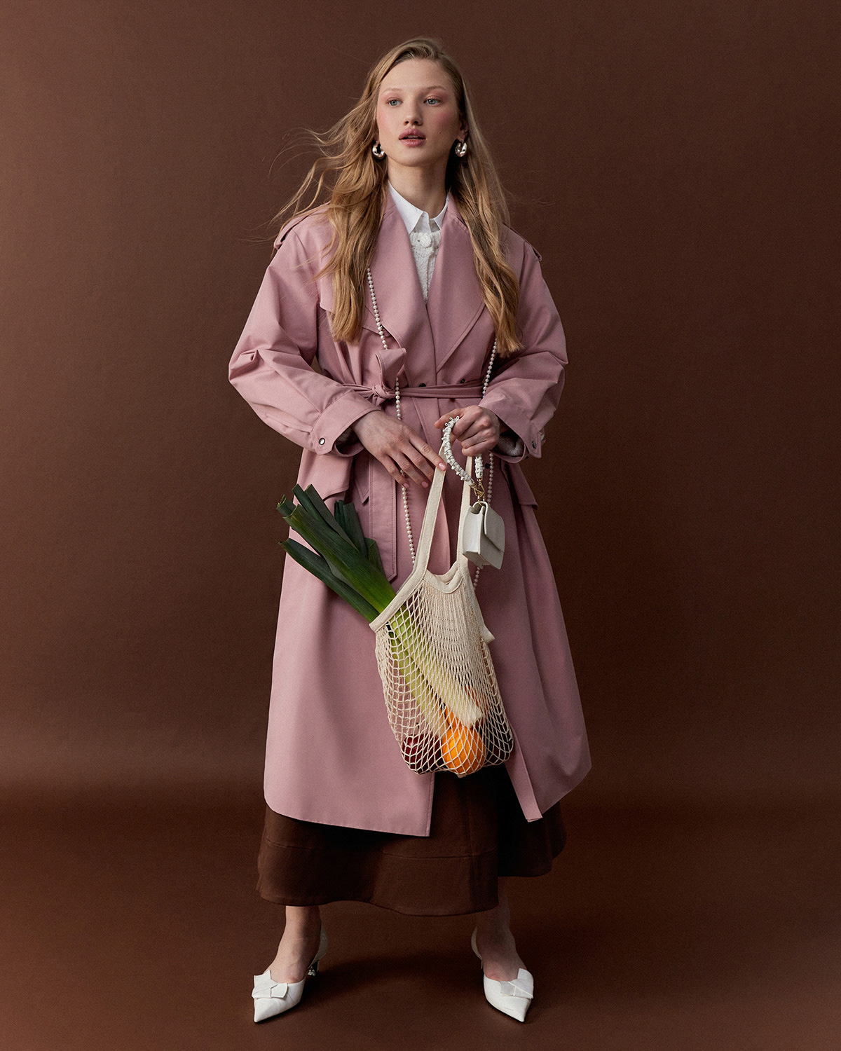 Onlyme Catalog — model in pink trench coat with pearl necklace holding mesh bag with vegetables
