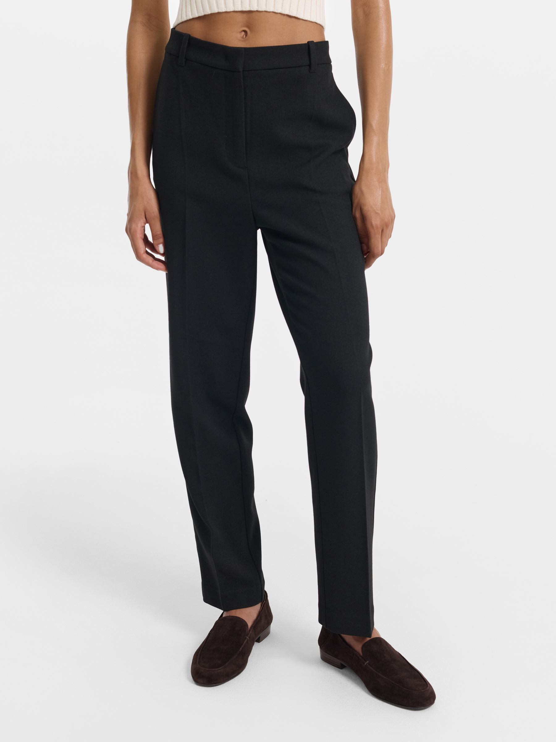 Before retouch — black tailored trousers with cream ribbed crop top and brown suede loafers on light background, raw product shot